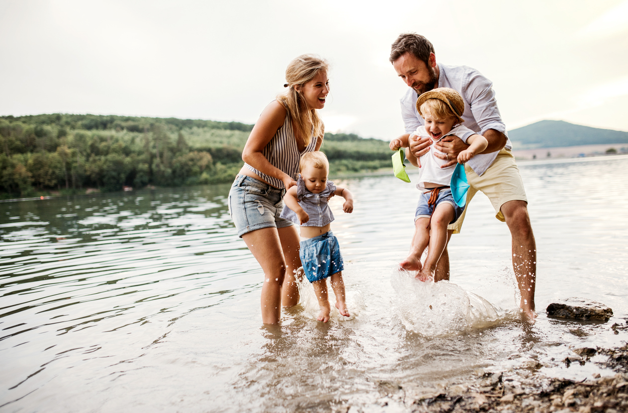 A young family with two toddlers splashing in the lake and laughing.