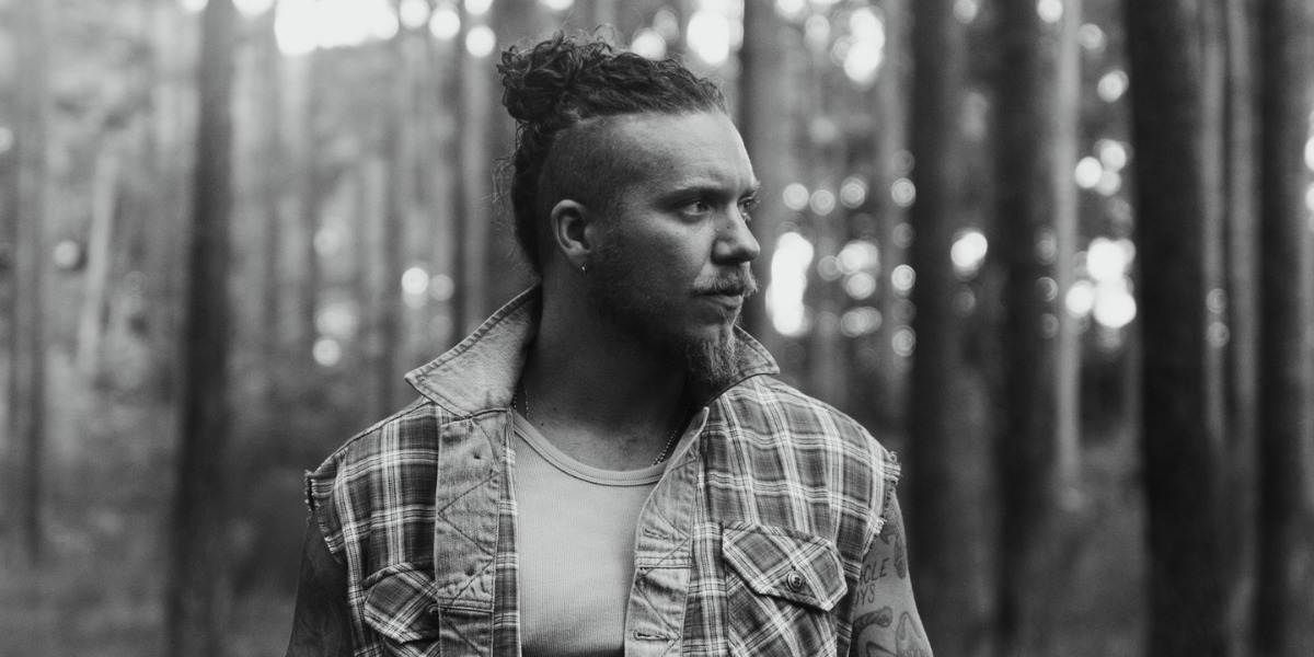 Brandon Lake in a forest. He's wearing plaid. The image is in greyscale