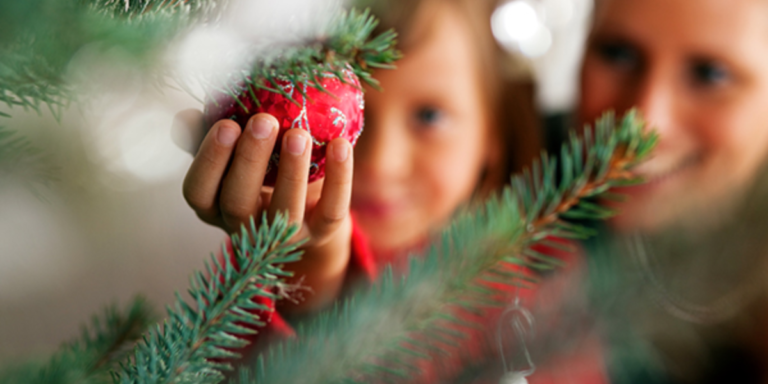 A little girl handing a red ornament on the tree with her mom