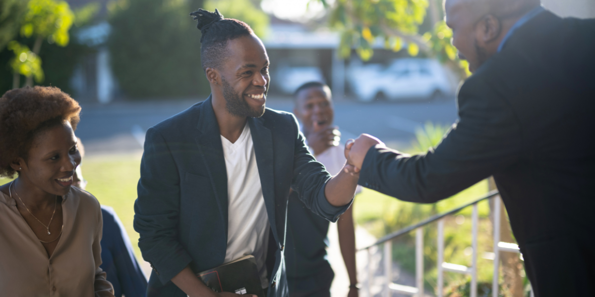 A pastor greeting smiling church members at the doorway of the church.